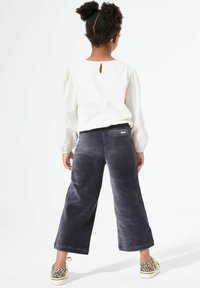 Grijze corduroy wijde broek met een achterzakdetail, gecombineerd met een witte blouse met lange mouwen en pantalon schoenen.