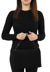 Borsa a pochette nera in suede con forma rettangolare, caratterizzata da una sottile tracolla e dettagli in oro, tenuta in mano davanti a uno sfondo bianco.