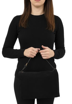 Borsa a pochette nera in suede con forma rettangolare, caratterizzata da una sottile tracolla e dettagli in oro, tenuta in mano davanti a uno sfondo bianco.