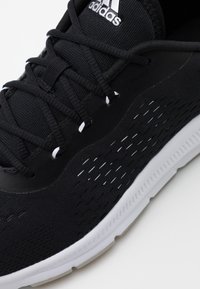 Primo piano di una scarpa da running nera Adidas con suola bianca e cuciture dettagliate su sfondo bianco.