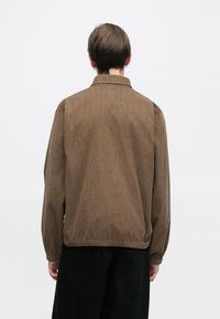 Brun kordfløyelsjakke med avslappet passform, med krage, elastiske mansjetter og rett nederkant. Strukturert overflate og minimalistisk design.