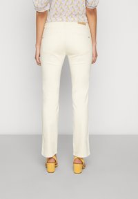Pantalones de mezclilla blancos acampanados con una cintura de altura media, corte recto y dos bolsillos traseros. Combinados con sandalias amarillas de tacón bloque.
