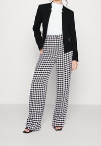 Veste noire à la silhouette ajustée, associée à un pantalon taille haute à jambes larges avec un motif pied-de-poule noir et blanc.