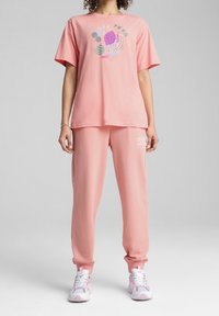 Rosa bomull T-shirt med tryck och matchande rosa sweatpants. Har en lös passform och mjuk textur. Sneakers med pastellfärger.