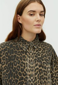 Denimová košile s leopardím potiskem, límečkem, zapínáním na knoflíky vpředu a jednou náprsní kapsou. Má strukturovanou tkaninu a tlumenou barevnou paletu.