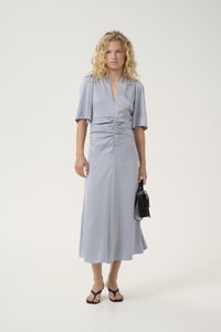 Light gray dress with short sleeves, gathered waist, and a flowy skirt. Worn with flat black sandals and a small black handbag.