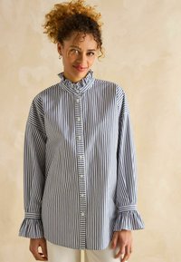 Sinise ja valge triibuline nööbitegija särk, millel on volangkrae ja laienevad varrukad, valmistatud kergest kangast.