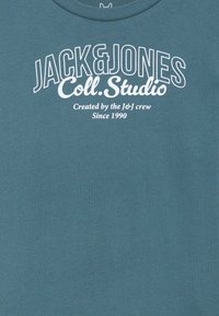 Mėlynas medvilninis marškinėlis su dideliais baltais užrašais: "JACK&JONES Coll.Studio" ir smulkiais užrašais žemiau. Apvali iškirptė ir trumpomis rankovėmis.