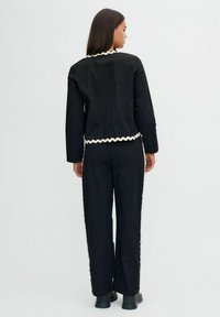 Completo giacca e pantaloni in cotone nero con bordo bianco a scallop lungo il colletto, l'orlo e le cuciture laterali. Design semplice e sartoriale.