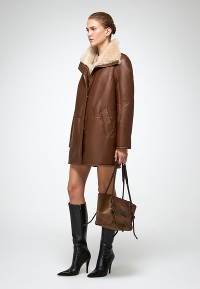 Bruine leren jas met een tan schapenvacht kraag, voorzien van grote voorkruimzakken en een rits aan de voorkant. Gemaakt in combinatie met knielange zwarte stiletto laarzen en een bruine handtas.