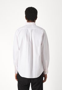 Camicia button-up rosa chiaro con un sottile motivo a righe verticali, maniche lunghe e pieghe sulle spalle, realizzata in un tessuto liscio.