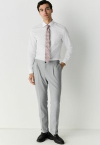 Weißes Hemd und hellgraue karierte Hose, mit einer pinkgemusterten Krawatte. Schwarze Slipper runden das Outfit ab. Maßgeschneiderte Passform und gerader Schnitt.