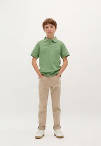 Polo en coton vert à manches courtes et col, associé à un pantalon beige et des baskets blanches, offrant une coupe décontractée.