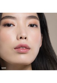 Primo piano di un volto con pelle chiara e liscia; labbra rosa pallido; e capelli scuri e lisci. Un trucco leggero evidenzia gli occhi e le guance.