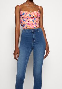 Blommig kort topp i rosa, orange och blått med puffad design; matchad med hög midja och åtsittande blå jeans. Slät yta, justerbara band.