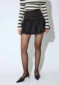 Jupe bouffante noire avec une taille ajustée, portée avec un haut rayé noir et blanc, des collants noirs et des escarpins à talon dans le même ton.