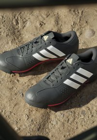 Dunkelgraue Sportschuhe mit weißen Streifen und roten Sohlen, die auf felsigem Boden im natürlichen Sonnenlicht ruhen.