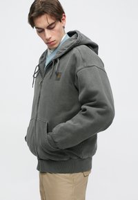 Γκρι φούτερ με φερμουάρ και κουκούλα με κορδόνι, πλαϊνές τσέπες και ribbed μανσέτες. Διαθέτει μια μικρή ετικέτα λογότυπου στο στήθος. Μαλακό, υφασμάτινο υλικό.