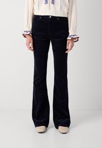 Marineblaue Corduroy-Flaggschiffhosen mit Eingrifftaschen und Reißverschluss, kombiniert mit einer cremefarbenen bestickten Bluse mit elastischen Bündchen.