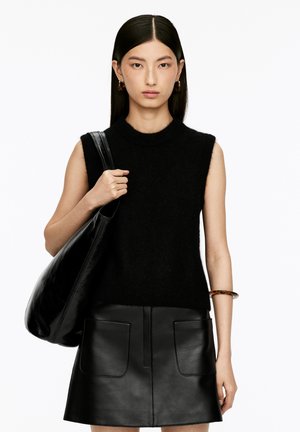 Black sleeveless knit top with a high neck, paired with a black leather mini skirt featuring front pockets. Model holds a large black bag.