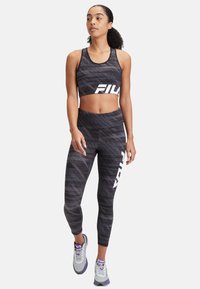 Sport-BH und Leggings in Schwarz und Grau mit einem weißen "FILA"-Logo; taillierte Passform; atmungsaktives Material; kombiniert mit grauen Turnschuhen.