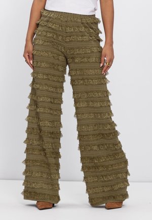 Olivengroene wijde broek met horizontale kanten ruches, gecombineerd met bruine puntige schoenen en een wit topje.