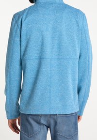 Giacca blu foderata in pile con colletto alto, maniche lunghe e un tessuto testurizzato. Presenta un taglio dritto e dettagli delle cuciture ben visibili.