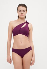 Completo bikini in un intenso viola, con reggiseno a spalla unica con dettaglio nodo e taglio, abbinato a slip a vita bassa. Materiale liscio e elastico.