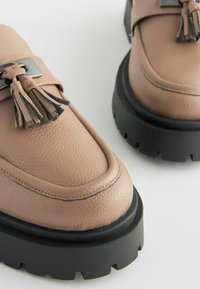 Mocassini in pelle beige con finitura texturizzata, dotati di dettagli a frange e una robusta suola nera platform.