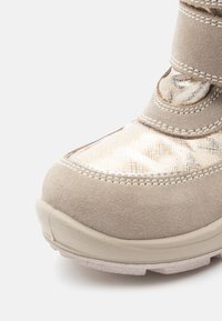 Bota de tornozelo bege com um corpo em camurça texturizada, painel têxtil com padrão, ponta reforçada e faixa ajustável com fecho de velcro para um ajuste seguro.