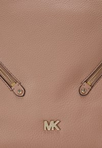 Sac à main en cuir texturé rose avec des fermetures éclair dorées et un logo doré en accent. Les fermetures éclair sont positionnées de manière symétrique à l'avant.