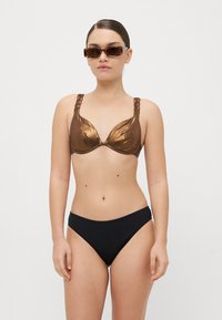 Smeđi metalik bikini top s pletenim trakama, uparen s crnim bikini gaćicama. Glatka tekstura s blagim sjajem.