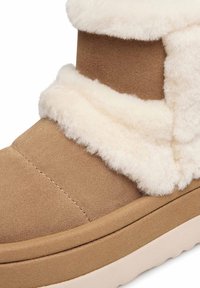 Sandfarbene Wildleder-Stiefelette mit dicker weißer Schaffellbesatz und einer beigefarbenen Gummisohle.