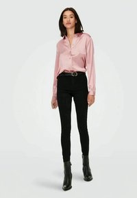 Camisa botões de cetim rosa claro, jeans skinny pretos de cintura alta, fivela de cinto prateada e botas pretas até o tornozelo com bico fino.