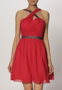 Red dress with a fitted bodice featuring horizontal pleats, crossed straps, and a textured skirt. Accented with a jeweled belt.