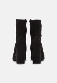Bottines en daim noir avec un talon épais haut. Dotées d'une fermeture éclair latérale et d'une texture lisse ; design élégant avec une silhouette ajustée.