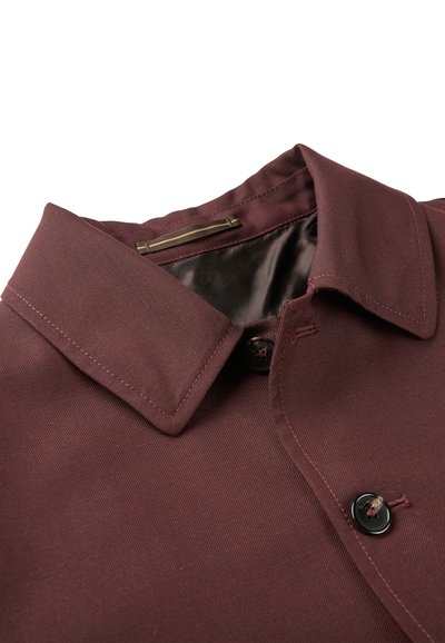 Chemise bordeaux avec un col pointu, deux boutons noirs et des coutures contrastées. Le tissu semble lisse avec une texture durable.