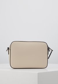 Beżowa prostokątna torba z teksturowanego materiału z czarnym zamkiem błyskawicznym i obramowaniem, wyposażona w dwa boczne paski ułatwiające noszenie.