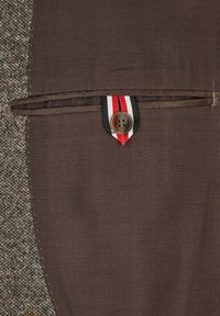 Brauner Stoffbeutel mit Knopfverschluss und gestreiftem Bandakzent; verfügt über eine subtile Textur und ein kontrastierendes Gewebemuster auf einer Seite.