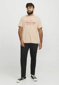 Světle broskvové tričko s červeným grafickým textem "JACK & JONES Surfer's Club". V kombinaci s černými kalhotami a černými teniskami.