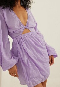 Lavendelfarbenes Minikleid mit tiefem V-Ausschnitt, verdrehtem Vorderteil und langen, luftigen Ärmeln. Verfügt über einen Ausschnitt in der Taille und eine zerknüllte Textur.