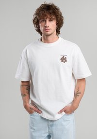 White cotton T-shirt with short sleeves, round neckline, and a small brown floral logo and "CALIFORNIA" text on the left chest.