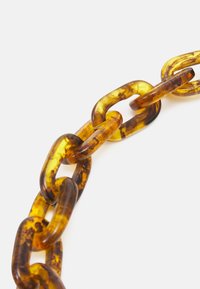 Průhledné řetězové články z jantarové barvy plastu s mramorovým vzorem na čistě bílém pozadí.