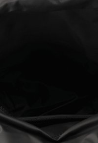 Interno di uno zaino nero con tessuto liscio e opaco. Presenta una tasca con zip lungo il lato, che offre un ampio scomparto non foderato.