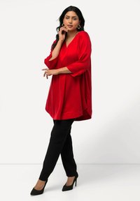 Rode tuniek met een V-hals en driekwart mouwen, gemaakt van gladde stof, gecombineerd met zwart slim-fit broek en gestructureerde zwarte hakken.