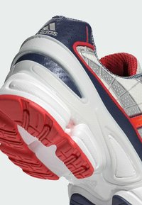 Adidas Sportschuh mit grauem und marineblauem Obermaterial, roten Akzenten, strukturierten Materialien und einer dicken weißen und roten Gummisohle.