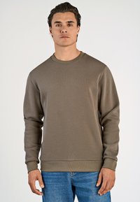 Sudadera marrón con cuello redondo y mangas largas. Textura suave y puños elásticos. Combinada con jeans desgastados de color azul claro.