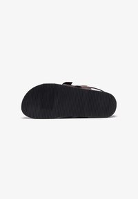 Black rubber sole with vertical ridges, featuring a smooth, brown leather strap design for secure fit and comfort.
