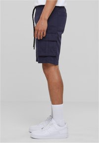Marine Cargo-Shorts mit mehreren Taschen, elastischem Bund und verstellbarem Kordelzug; kombiniert mit weißen Sneakers und Socken.