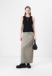 Top nero senza maniche con scollatura in rete, gonna lunga in denim azzurro chiaro, stivali platform neri e una piccola borsa nera.